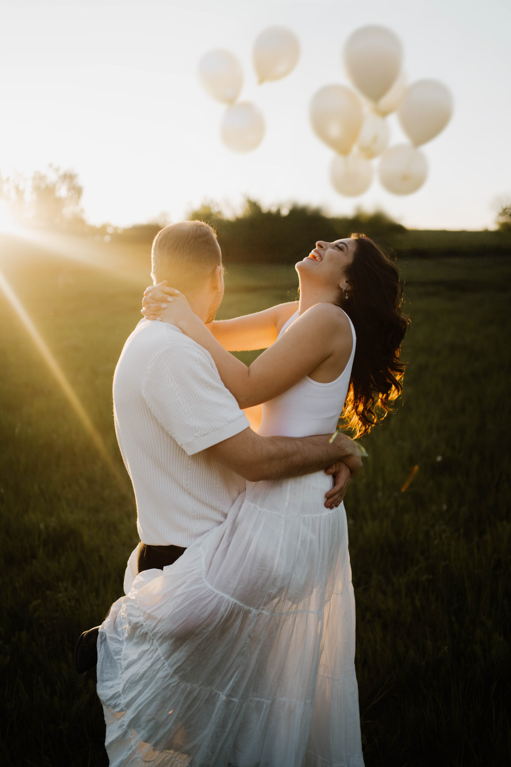 Paar bei Sonnenuntergang in Berlin lachend im weißen Kleid und Anzug. Im Hintergrund Hochzeitsballoons Hochzeitsfotografie in Berlin & Brandenburg