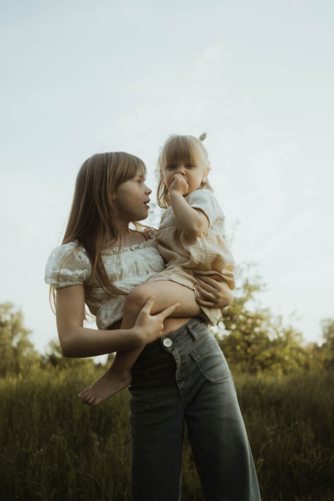 Große Schwester hält kleine Schwester auf dem Arm im Sommer Familienfotografie in Berlin & Brandenburg