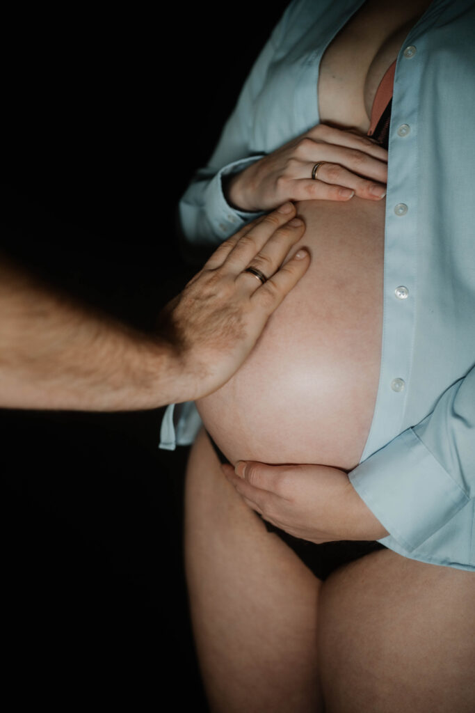 Mann mit Ehering berührt den schwangeren Bauch seiner Frau