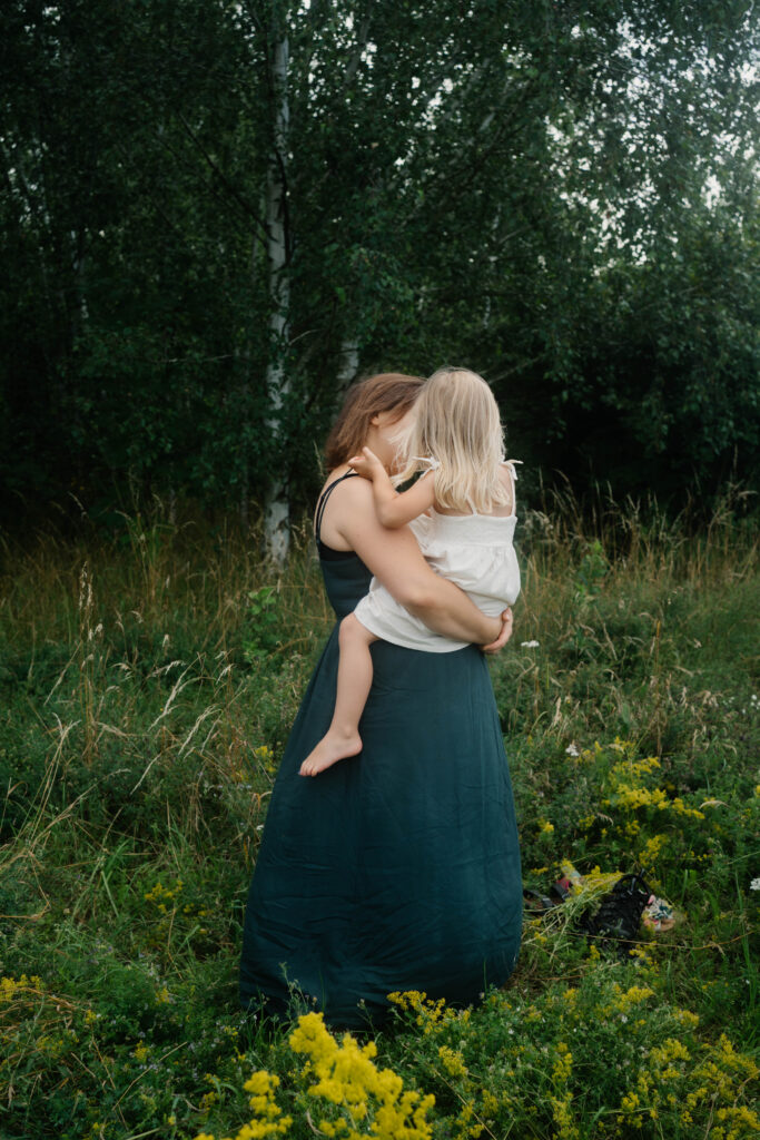 Mutter mit ihrer Tochter auf dem Arm im Grünen Familienfotografie in Berlin & Brandenburg