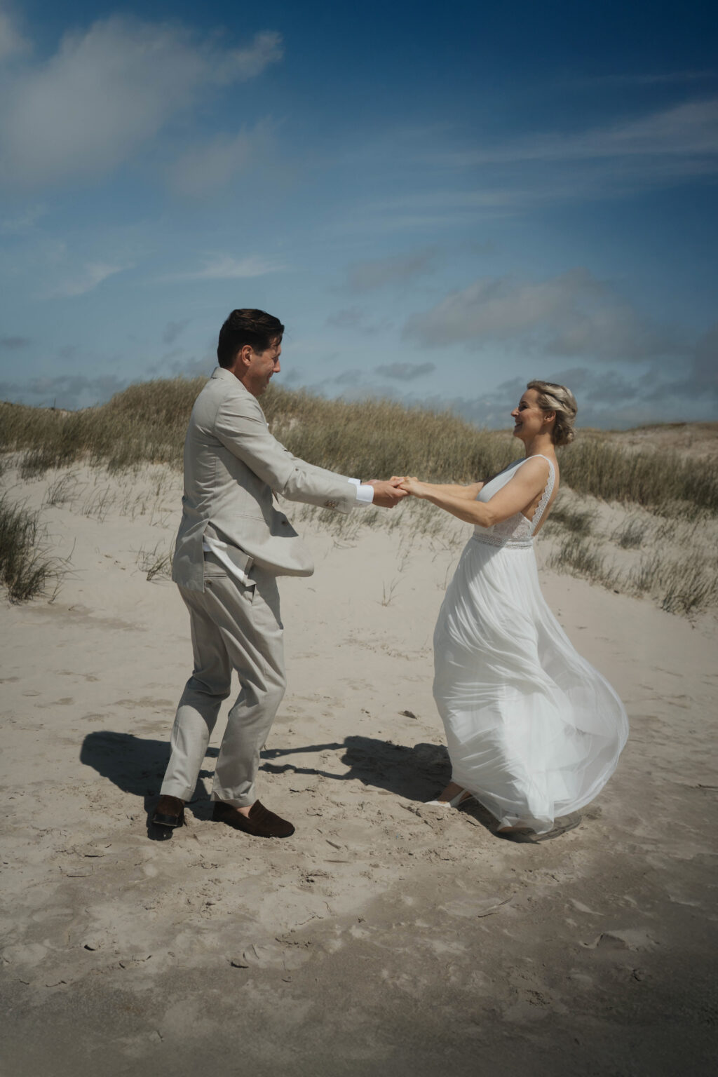 Hochzeitspaar mit beidem Anzug und weißem Kleid drehen sich am Strand Hochzeitsfotografie in Berlin & Brandenburg