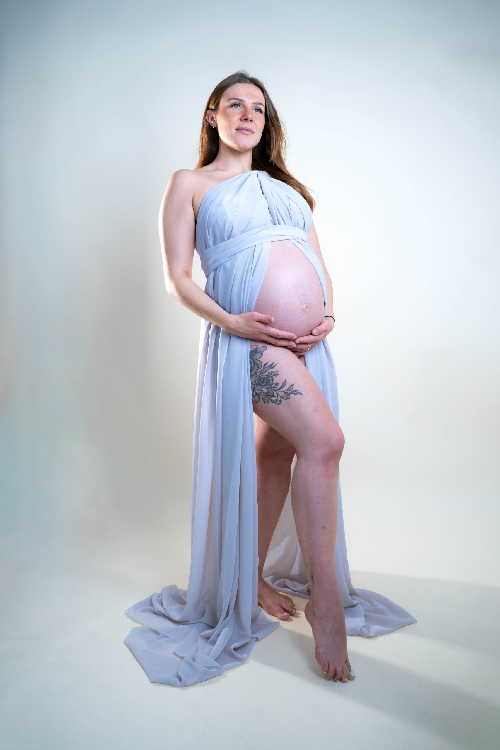 Schwangere Frau mit Babybauch bei einem Schwangerschaftsshooting mit langem blauen Kleid