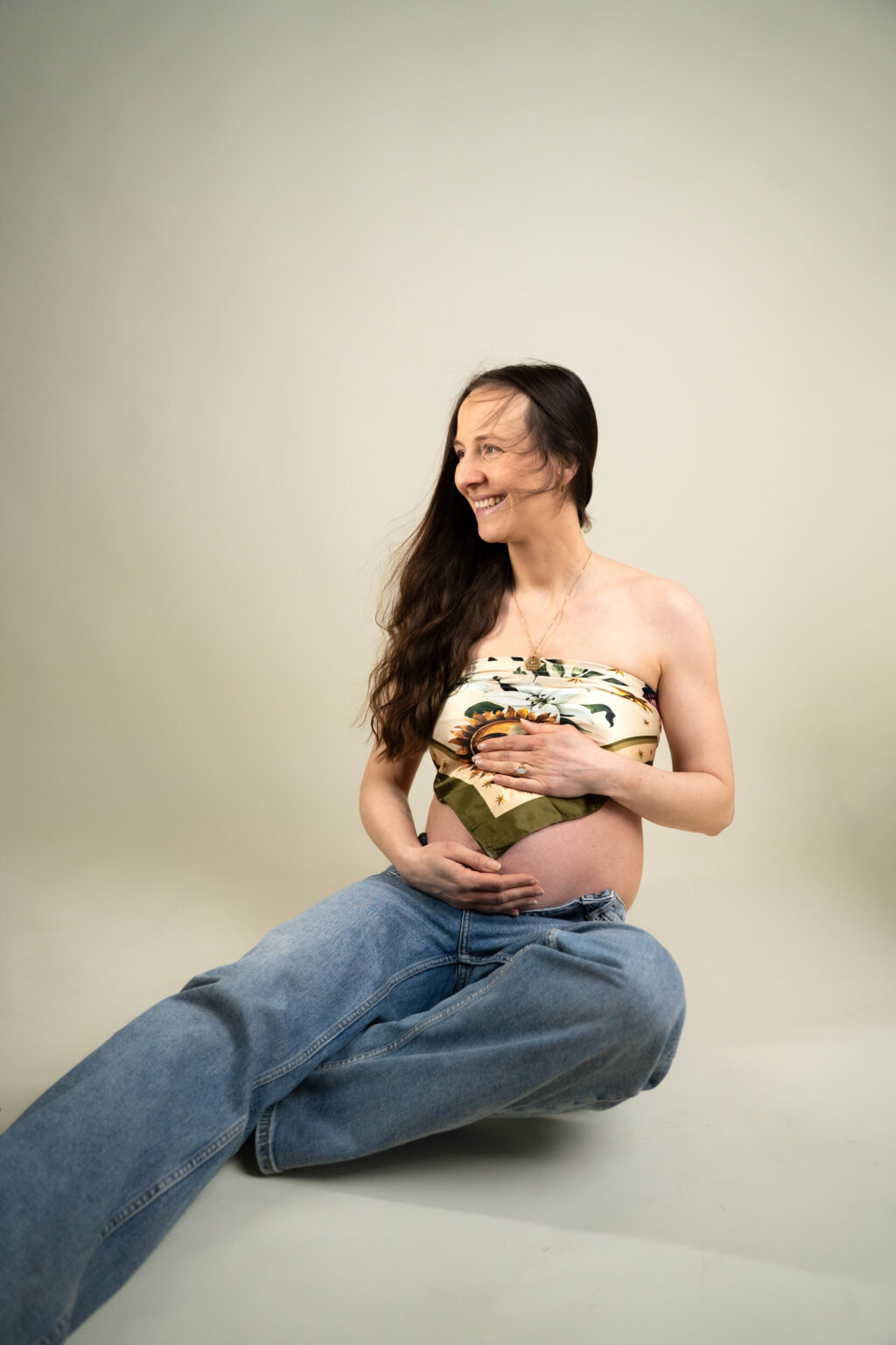 junge Frau mit Babybauch sitzend Haare wehen im Wind