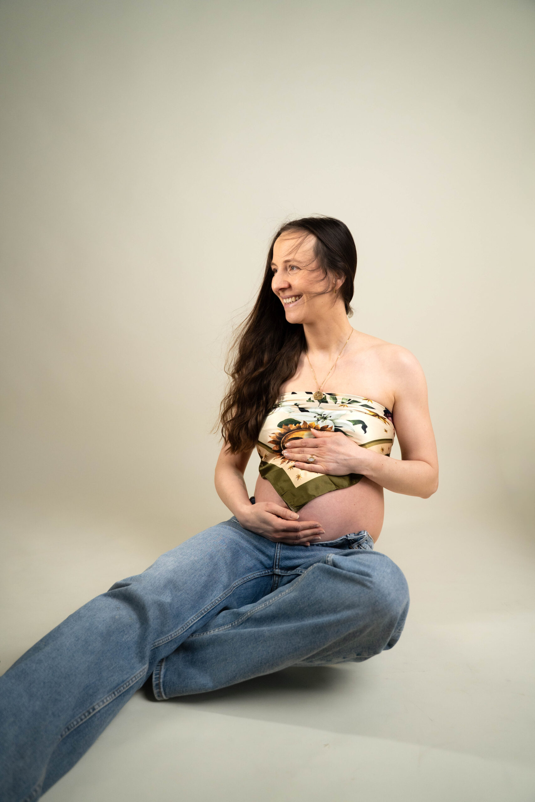 junge Frau mit Babybauch sitzend Haare wehen im Wind