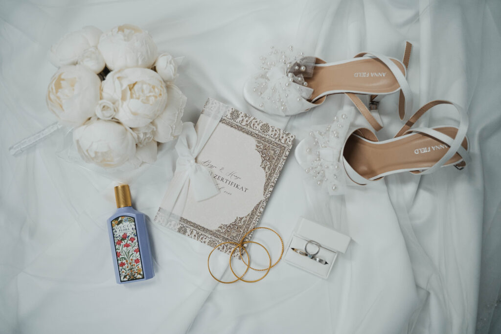Flatlay einer Hochzeit mit Brautstrauß, Schuhen und Schmuck
