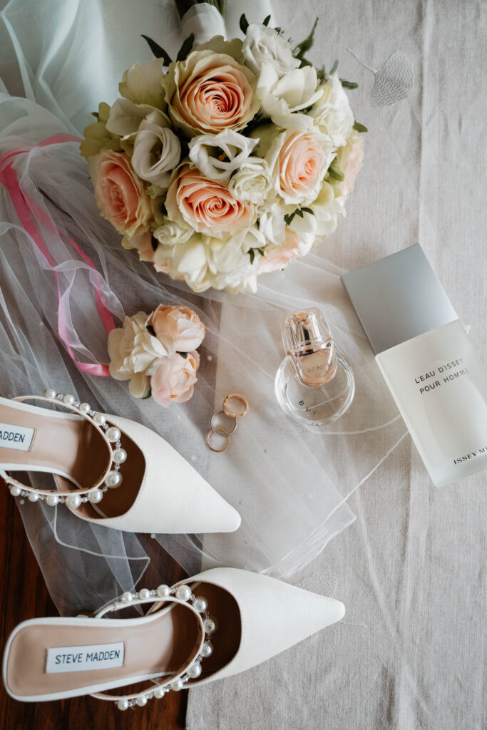 Flatlay einer Hochzeit mit Schuhen, Ringen, Parfüm und Brautstrauß