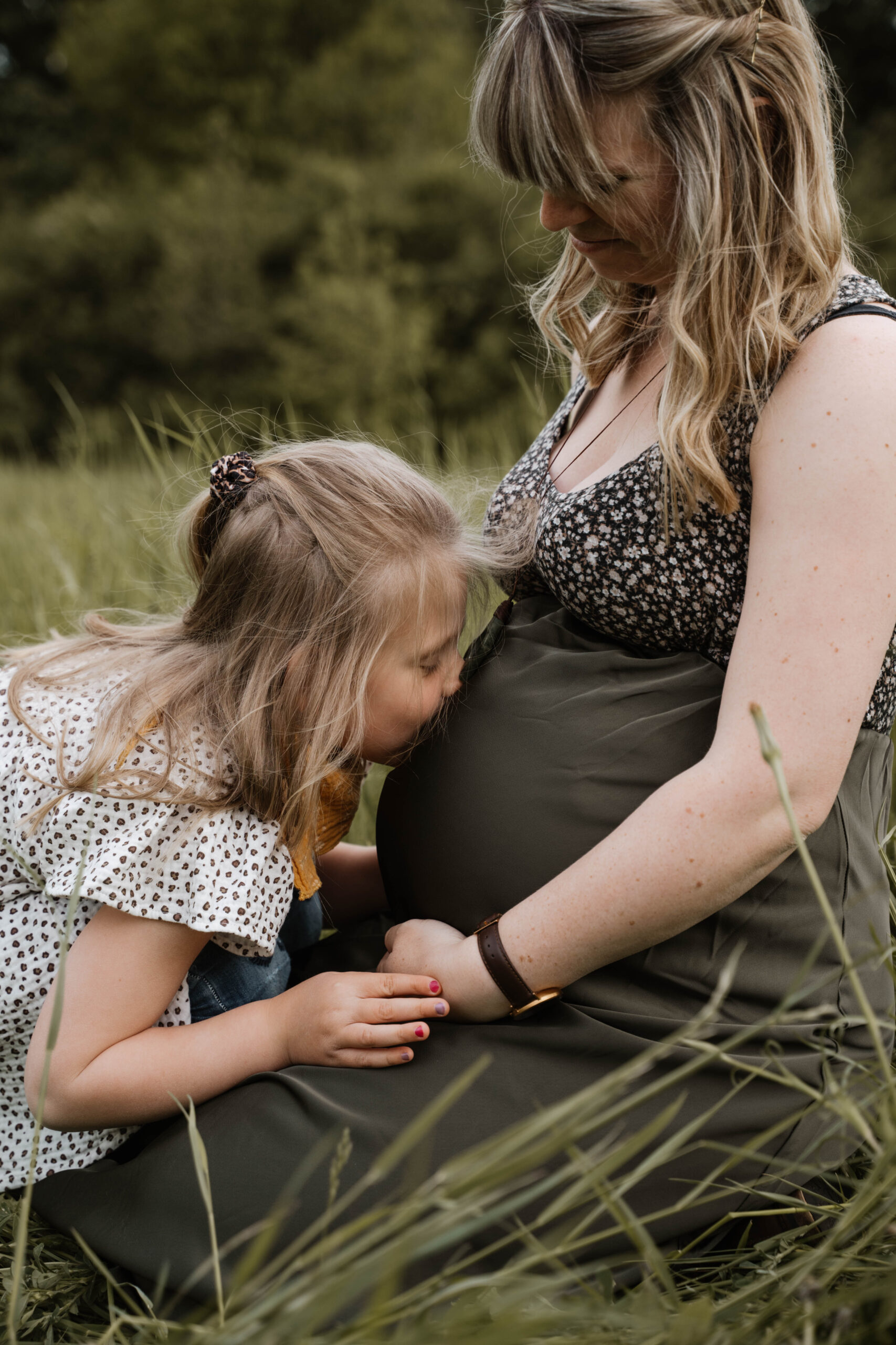 Kleines Mädchen küsst schwangeren Bauch der Mutter in der Natur